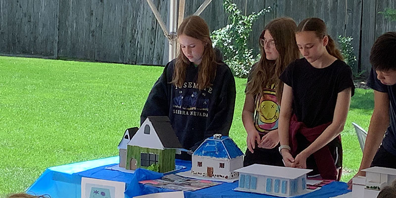 Middle school campers stand behind their completed models and architect’s logos