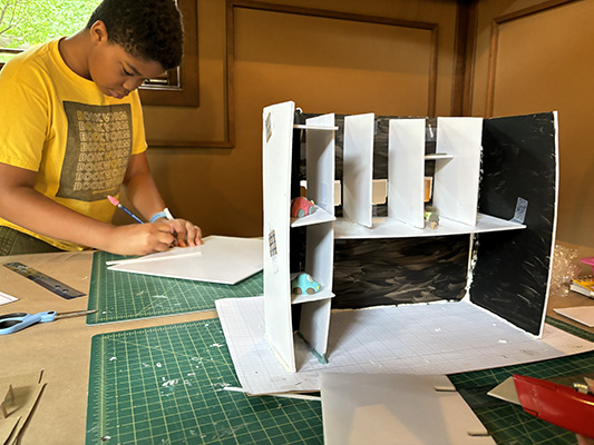 A close-up view of a camper's parking garage, while another camper measures his model's walls in the background.